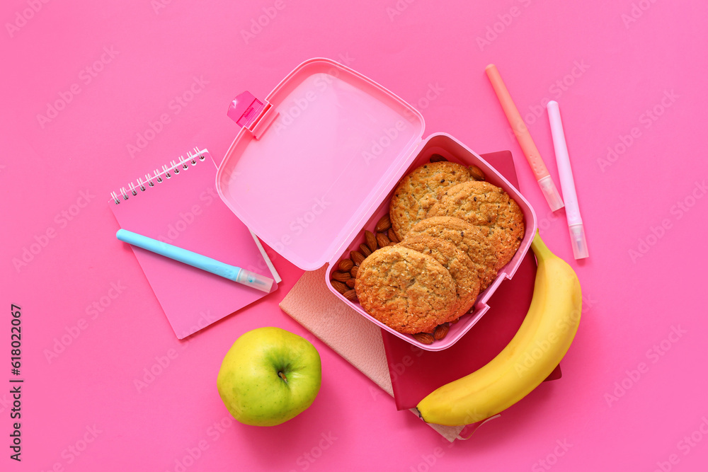 Stationery and lunch box with tasty food on pink background