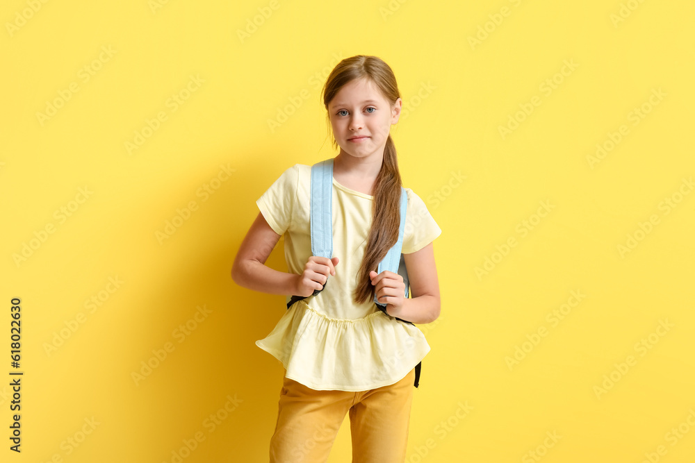 Little girl with backpack on yellow background