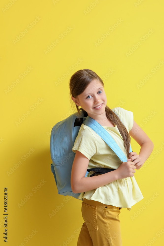 Little girl with backpack on yellow background