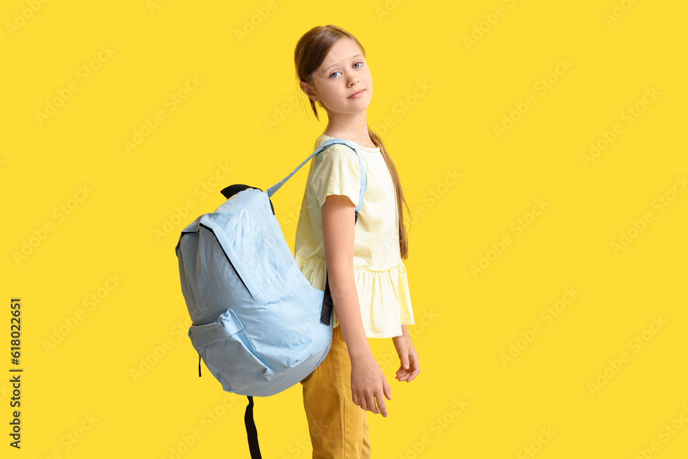 Little girl with backpack on yellow background