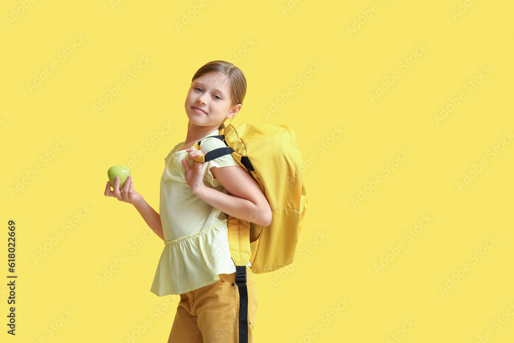 Little girl with apple and backpack on yellow background