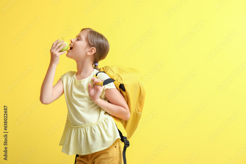 Little girl with apple and backpack on yellow background