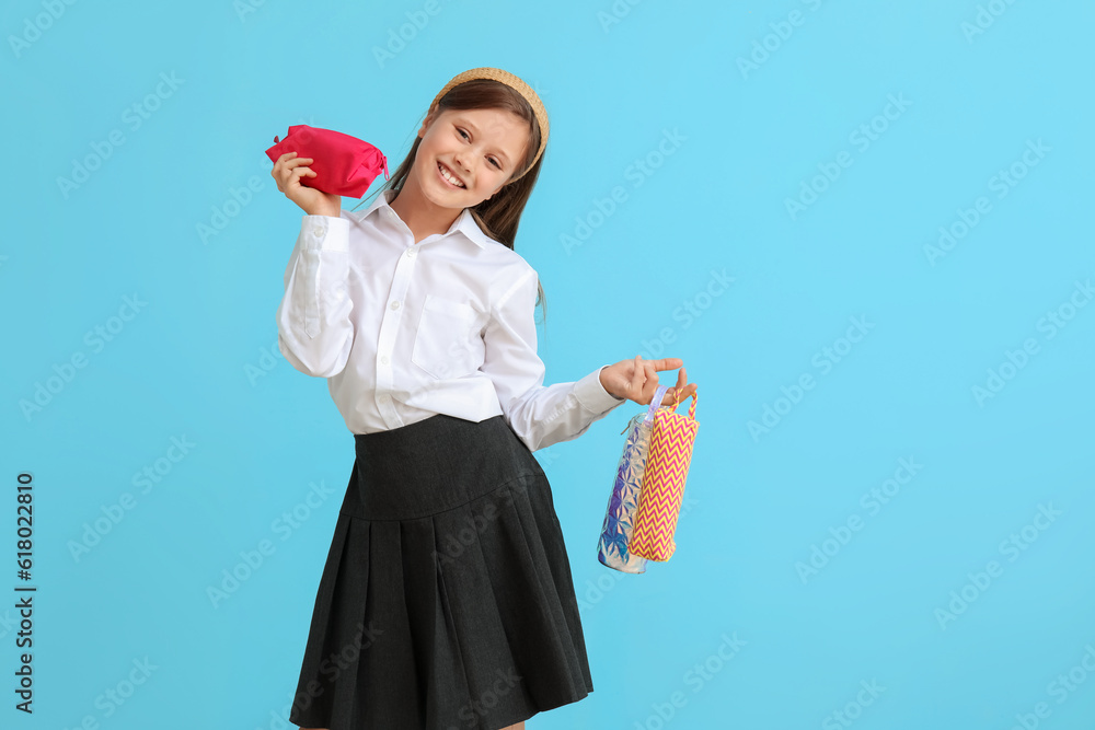 Little schoolgirl with pencil cases on blue background