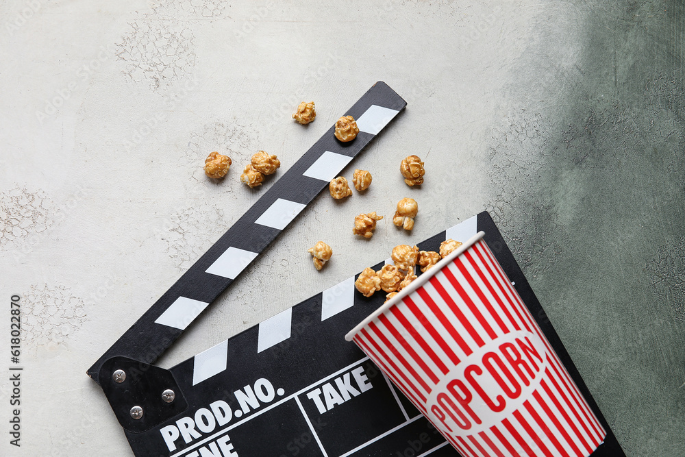 Bucket with tasty popcorn and clapperboard on grey background