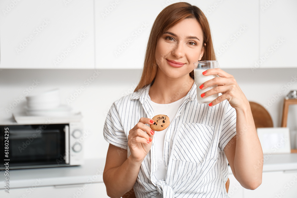 Young woman with glass of milk and cookie in kitchen