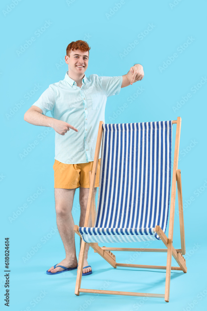 Young man pointing at deck chair on blue background