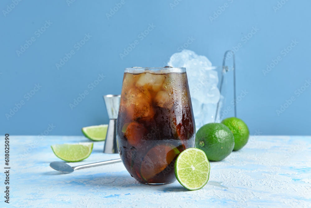 Glass of cold Cuba Libre cocktail on blue background