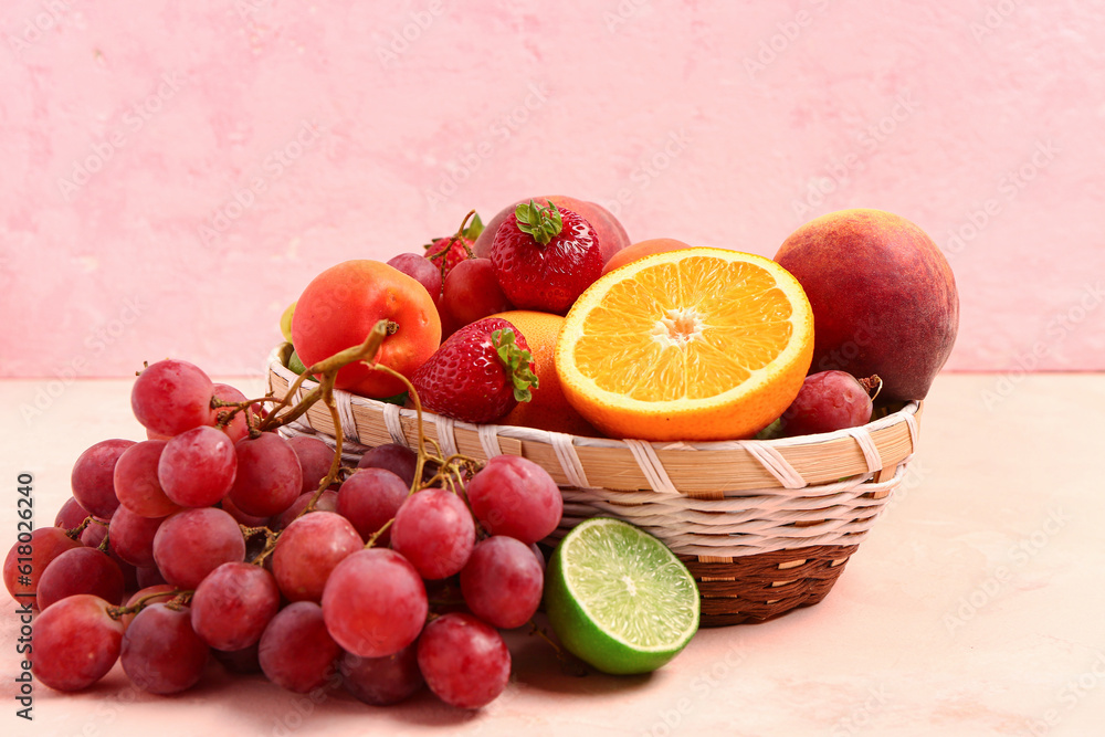 Wicker bowl with different fresh fruits on pink background