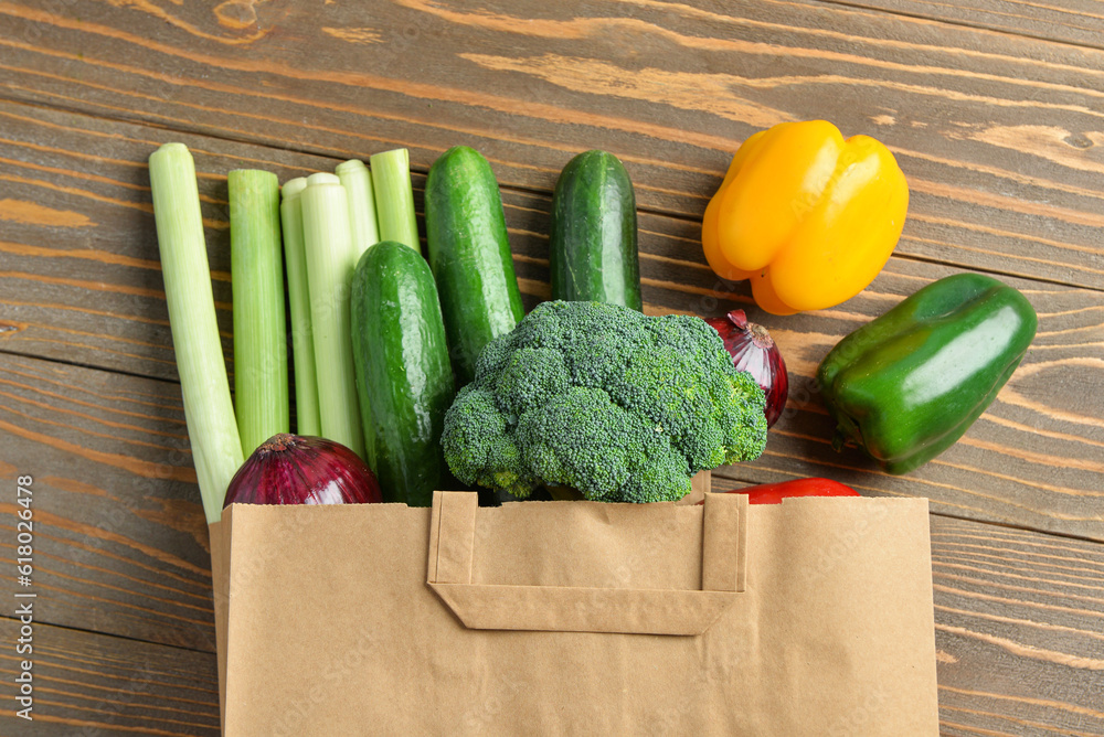 Paper bag with different vegetables on wooden background