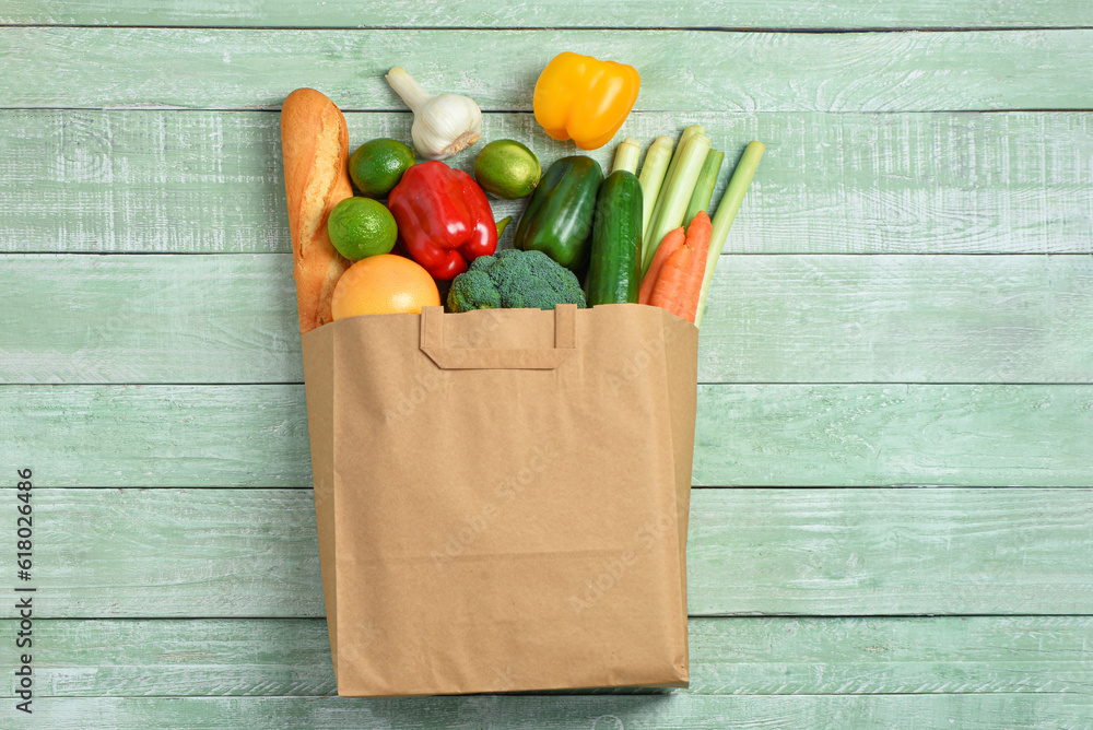 Paper bag with different products on green wooden background