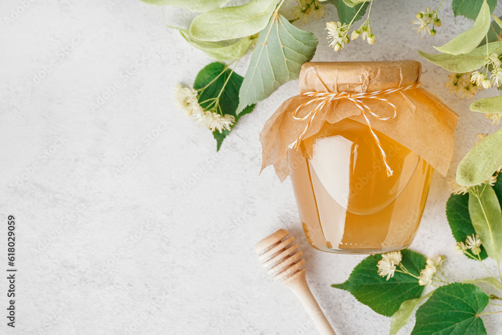 Glass jar with linden honey and dipper on light background