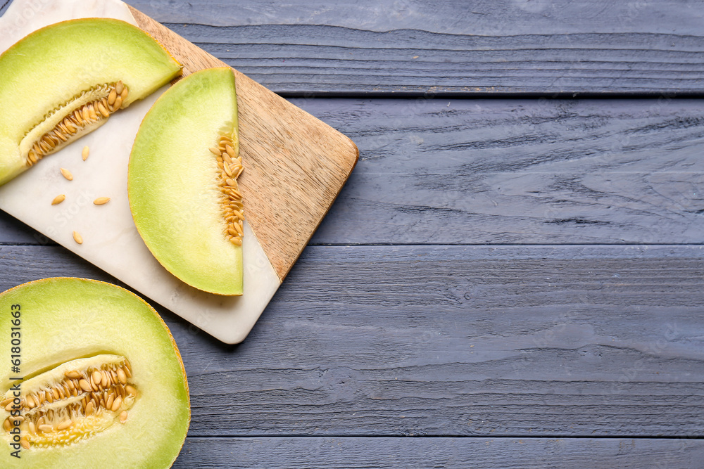 Half of sweet melon and board with pieces on blue wooden background