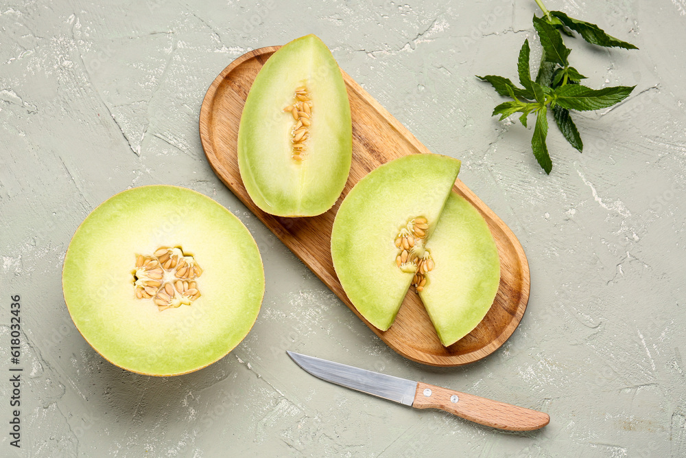 Half of sweet melon and wooden board with pieces on grey background