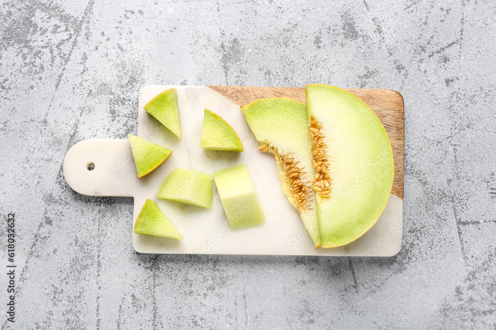 Board with pieces of sweet melon on grey background