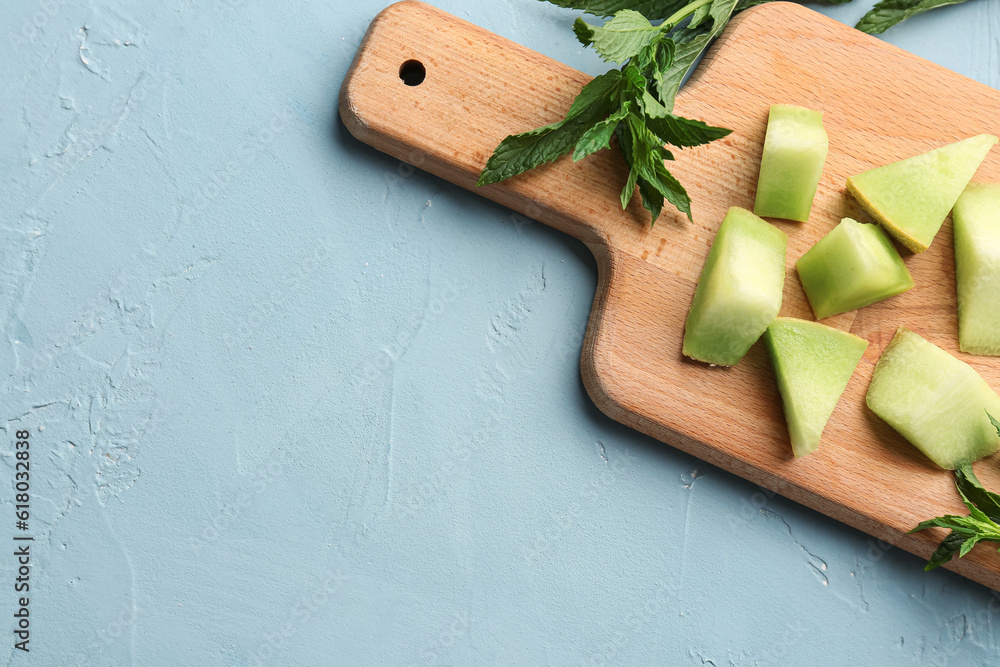 Wooden board with pieces of sweet melon and mint on blue background