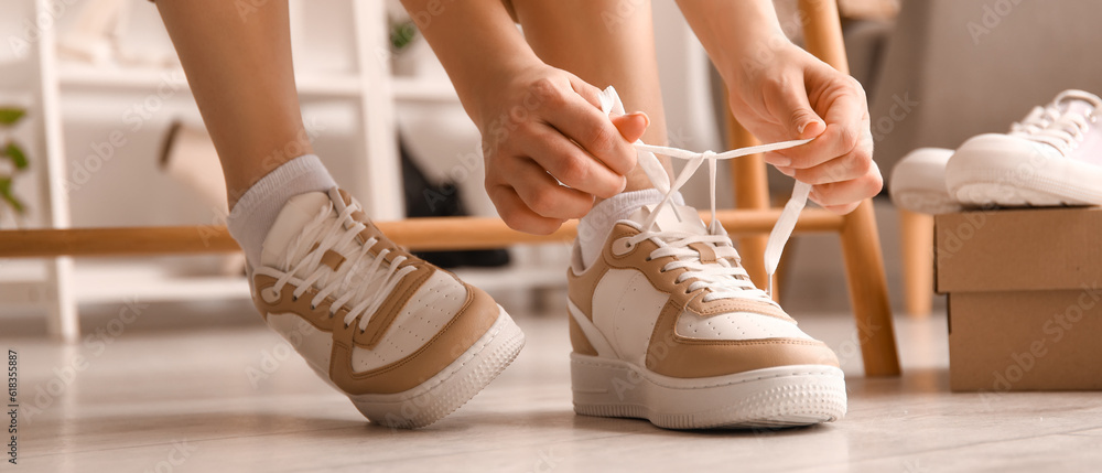 Woman in stylish sneakers tying shoe laces in shop