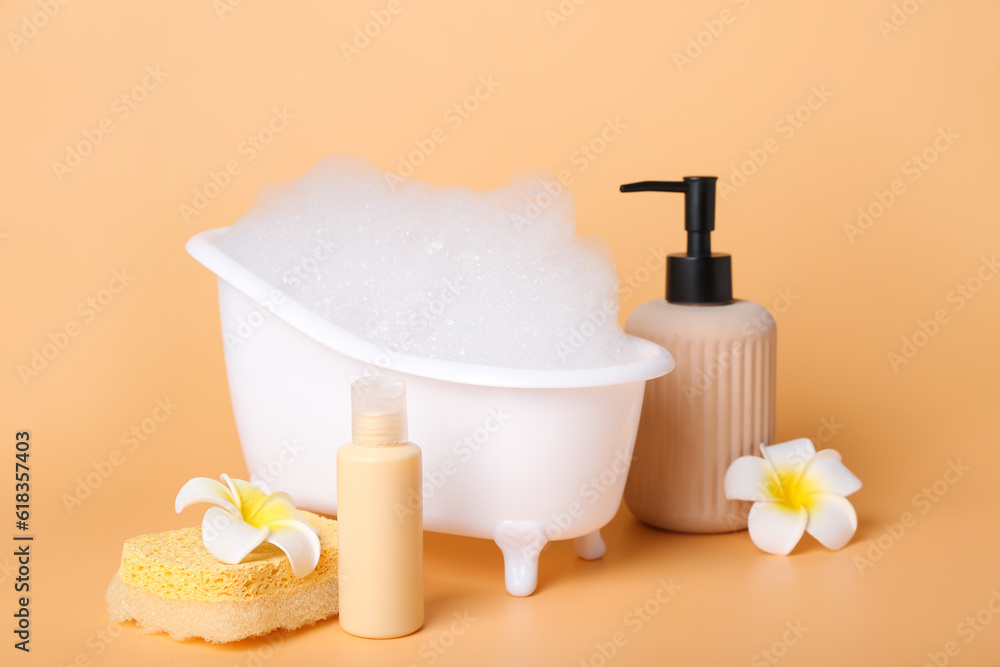 Small bathtub with foam, cosmetic products and flowers on color background