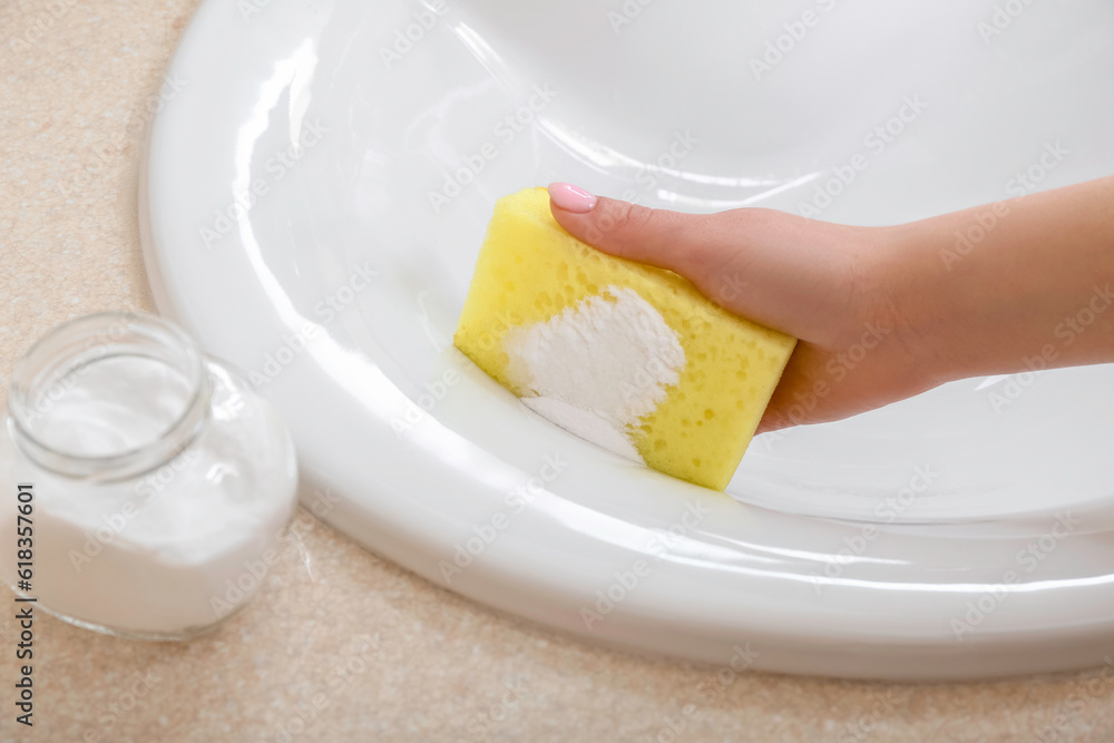 Woman cleaning white ceramic sink with sponge and baking soda, closeup