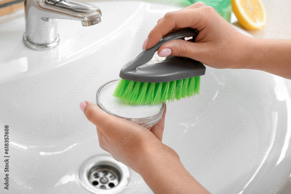 Woman cleaning white ceramic sink with brush and baking soda, closeup