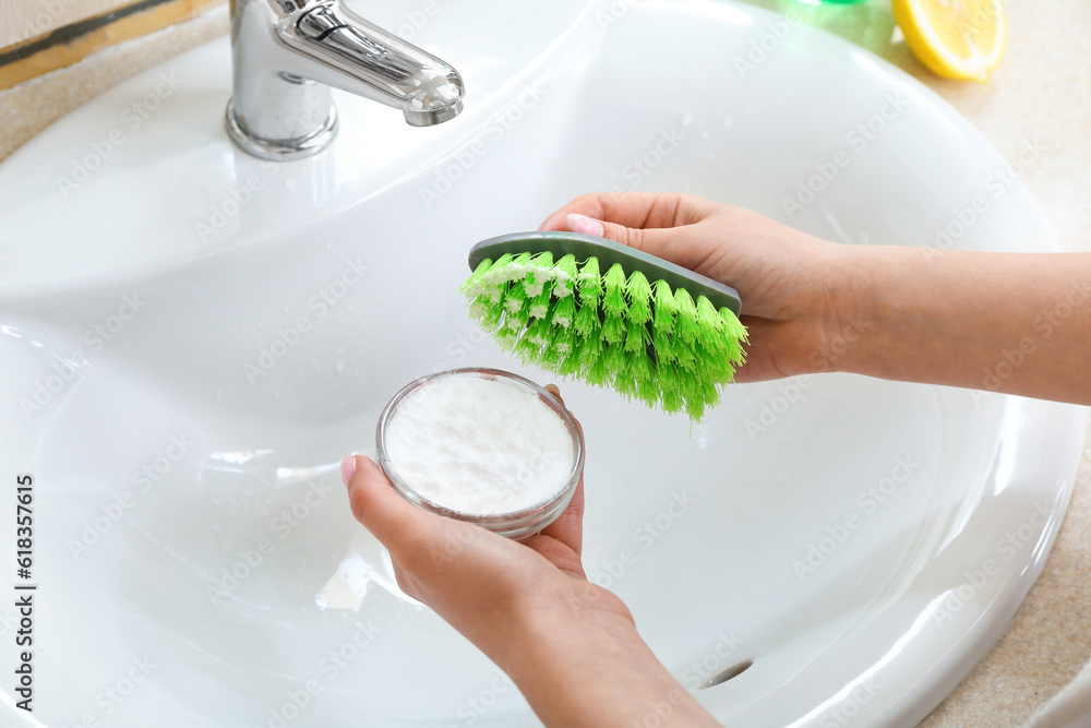 Woman cleaning white ceramic sink with brush and baking soda, closeup