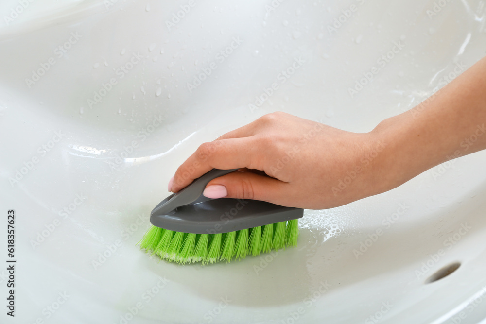 Woman cleaning white ceramic sink with brush and baking soda, closeup