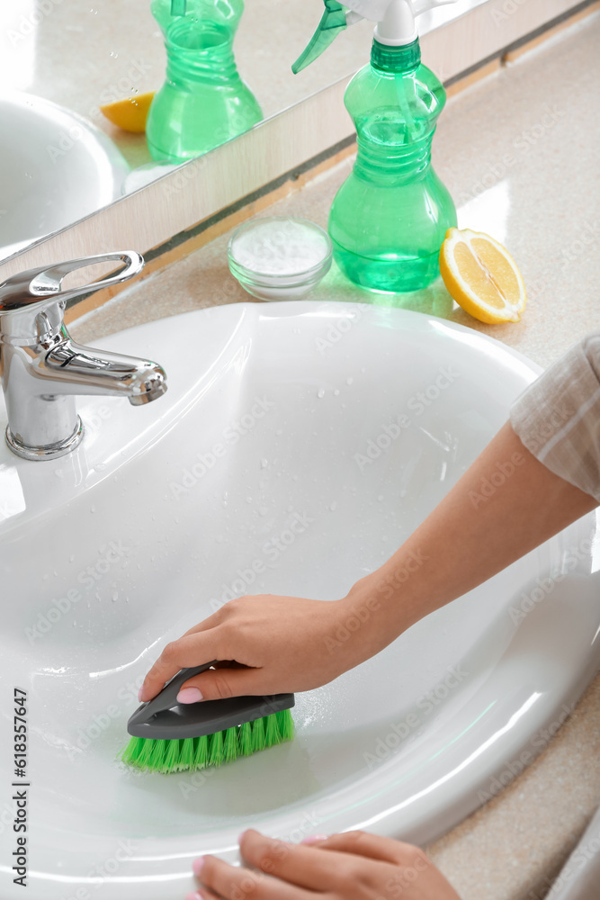 Woman cleaning white ceramic sink with brush and baking soda, closeup