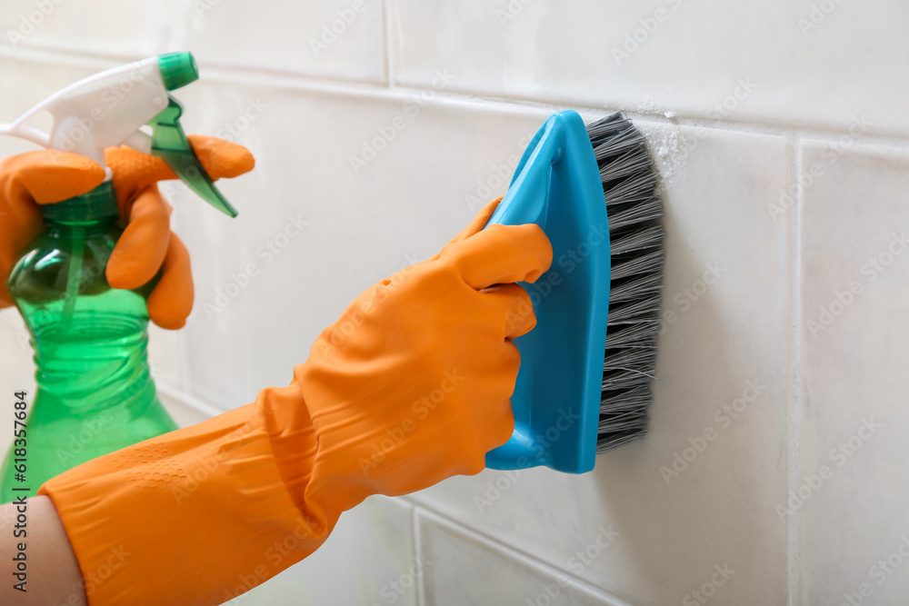 Woman in rubber gloves cleaning light tile with brush, baking soda and sprayer, closeup