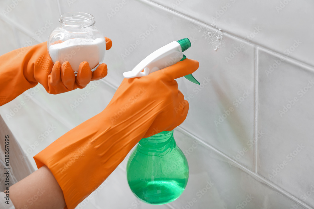 Woman in rubber gloves cleaning light tile with baking soda and sprayer, closeup