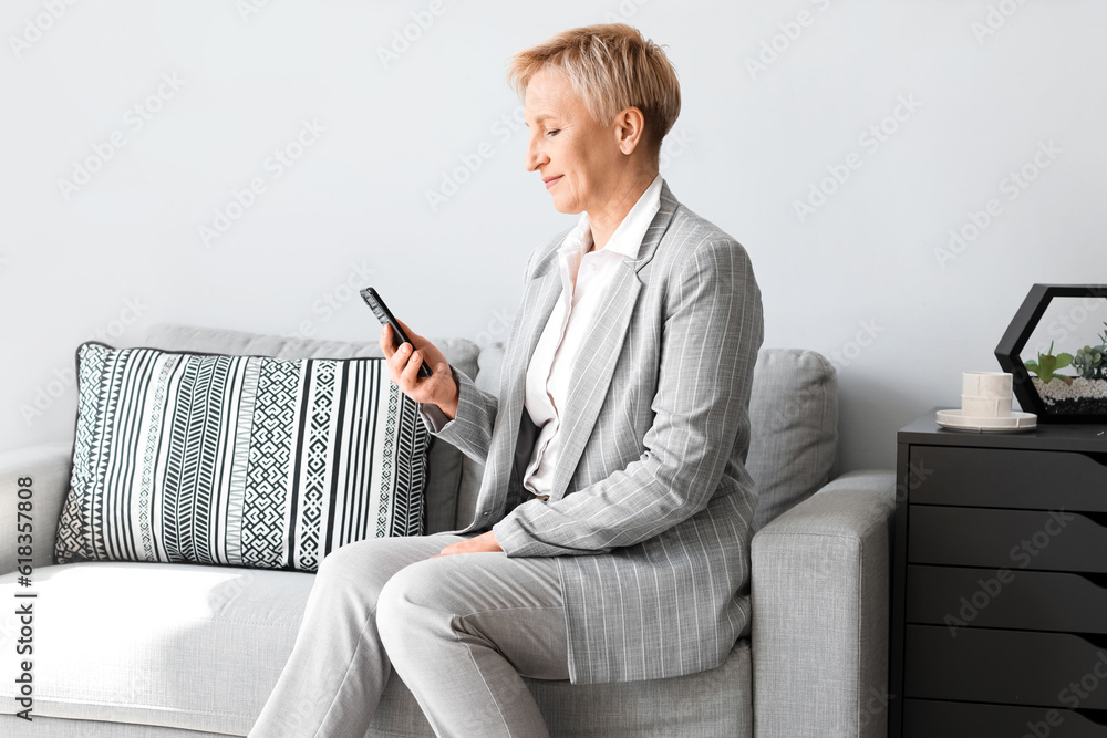 Mature businesswoman with mobile phone sitting on sofa in office