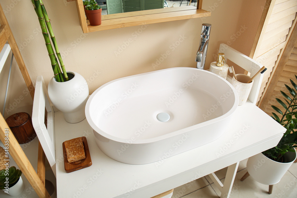 White sink, bath accessories and vase with bamboo stems on table in room