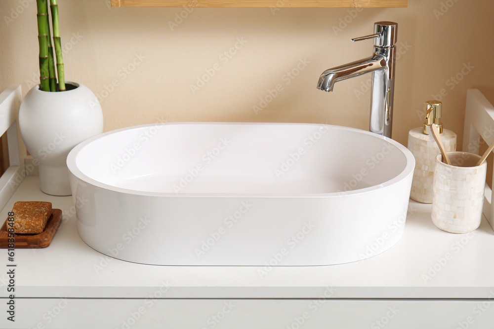 White sink, bath accessories and vase with bamboo stems on table in room