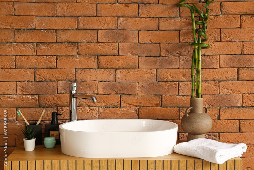 Sink, bath accessories and vase with bamboo stems on table in room