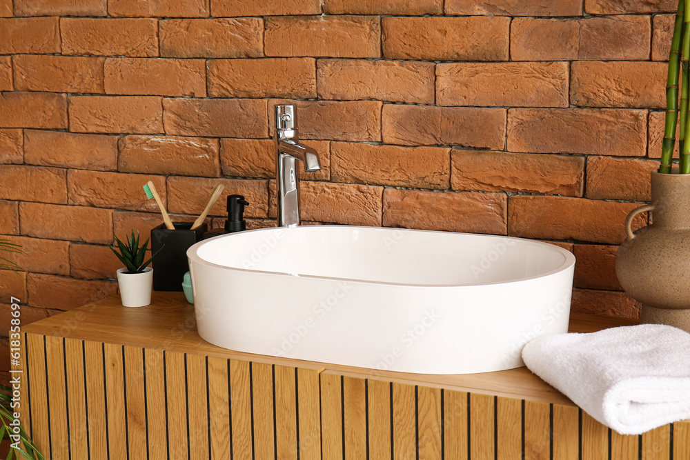 Sink with bath accessories on table near brick wall