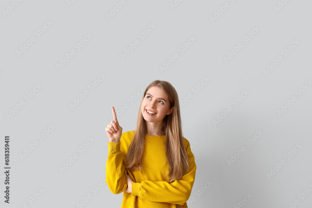 Thoughtful young woman pointing at something on light background