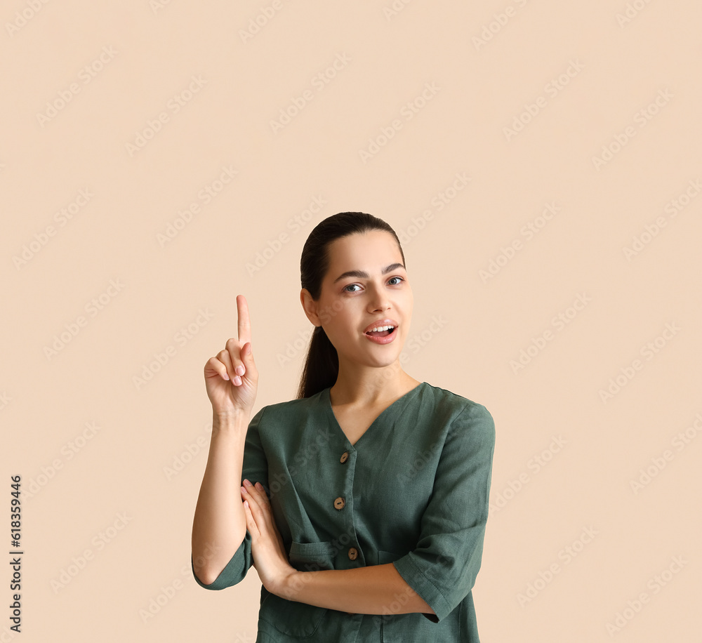 Thoughtful young woman pointing at something on beige background