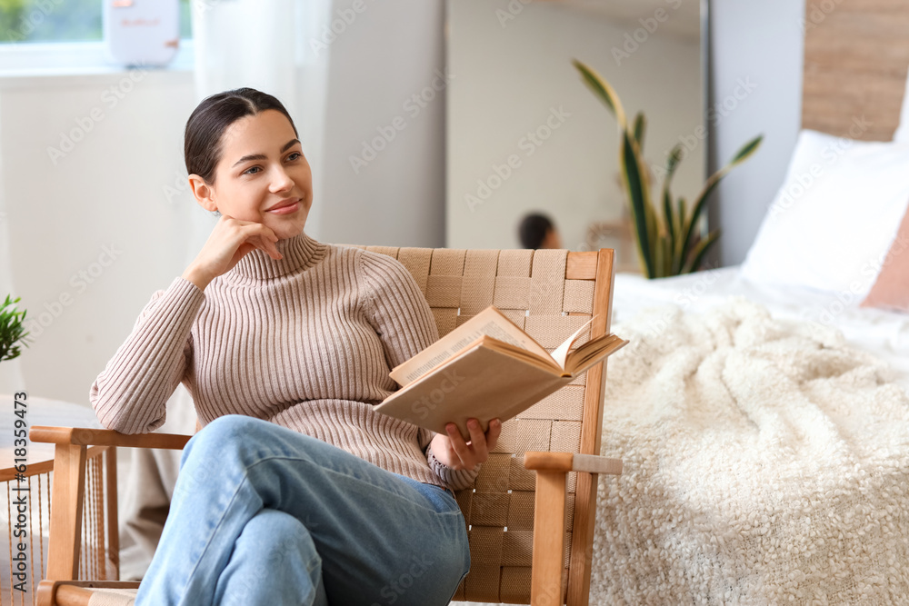 Dreaming young woman with book in armchair at home