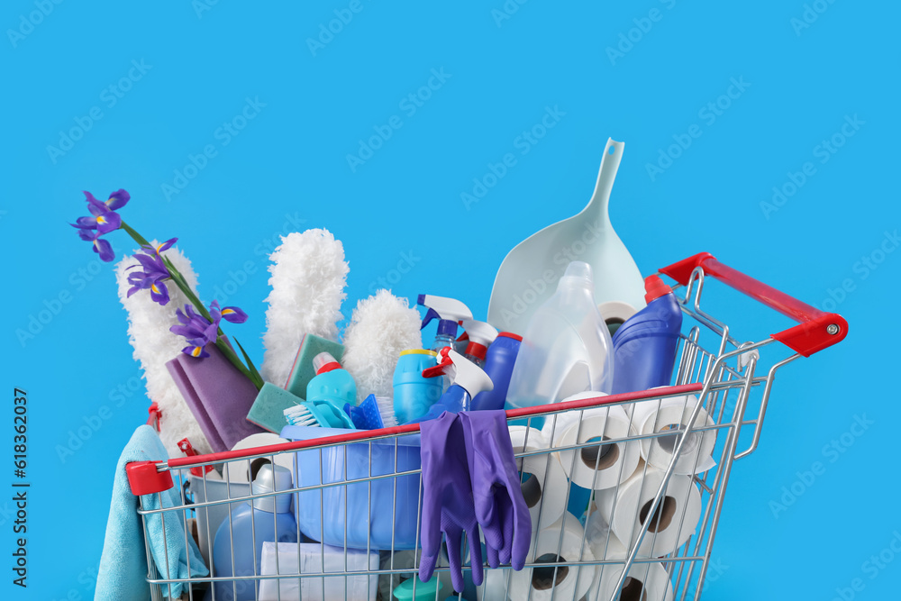 Shopping cart full of cleaning supplies and purple flowers on blue background