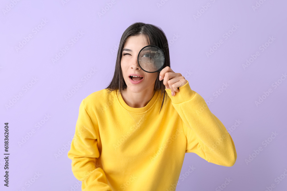 Beautiful shocked young woman with magnifier on lilac background