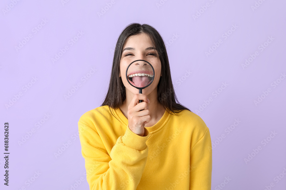 Beautiful happy young woman with magnifier showing tongue on lilac background