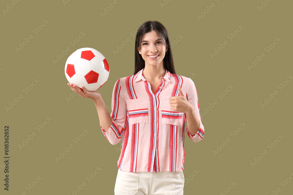 Young woman with soccer ball showing thumb-up on color background