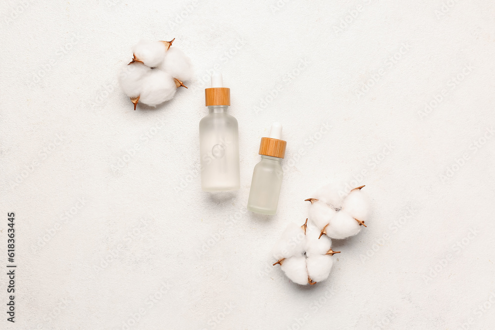 Bottles of essential oil and cotton flowers on light background