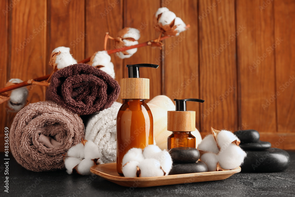 Composition with bottles of cosmetic products, bath supplies and cotton flowers on dark table agains