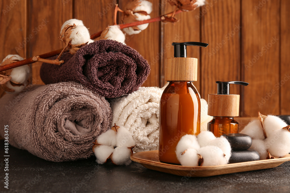 Composition with bottles of cosmetic products, bath supplies and cotton flowers on dark table agains