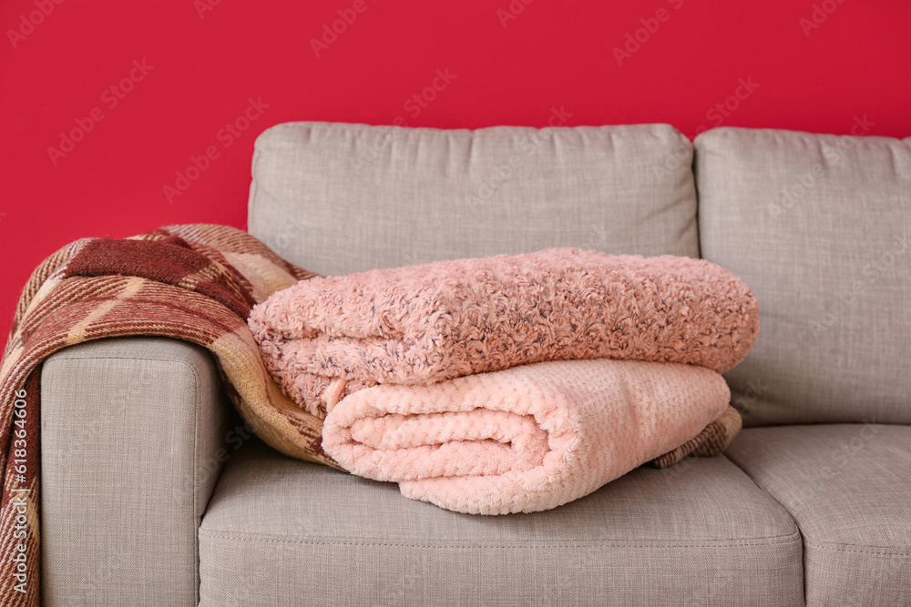 New soft blankets on sofa on burgundy background, closeup