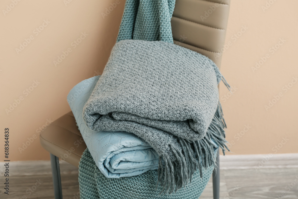 New soft folded blankets on chair near beige wall in room, closeup