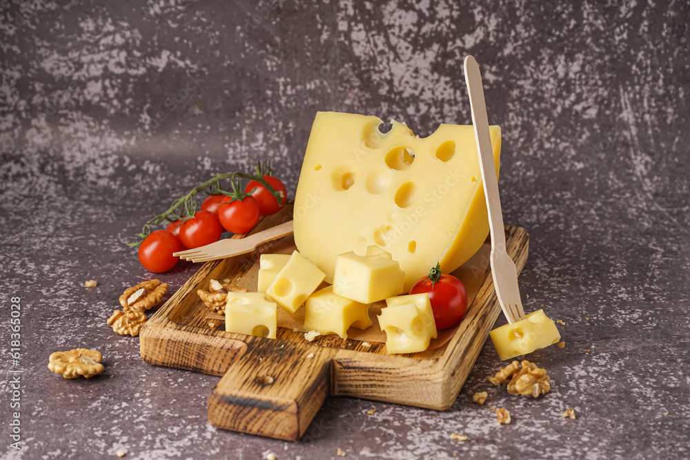 Board with pieces of Swiss cheese and tomatoes on grey background