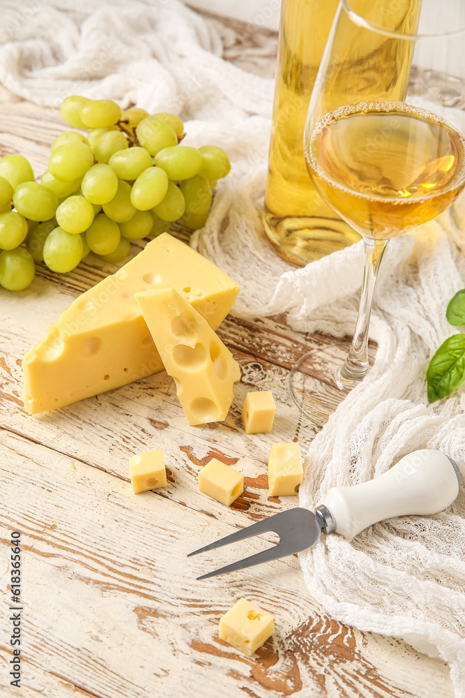 Tasty Swiss cheese, glass of wine and grapes on light wooden background