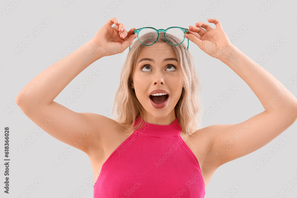 Surprised young woman in stylish eyeglasses on light background