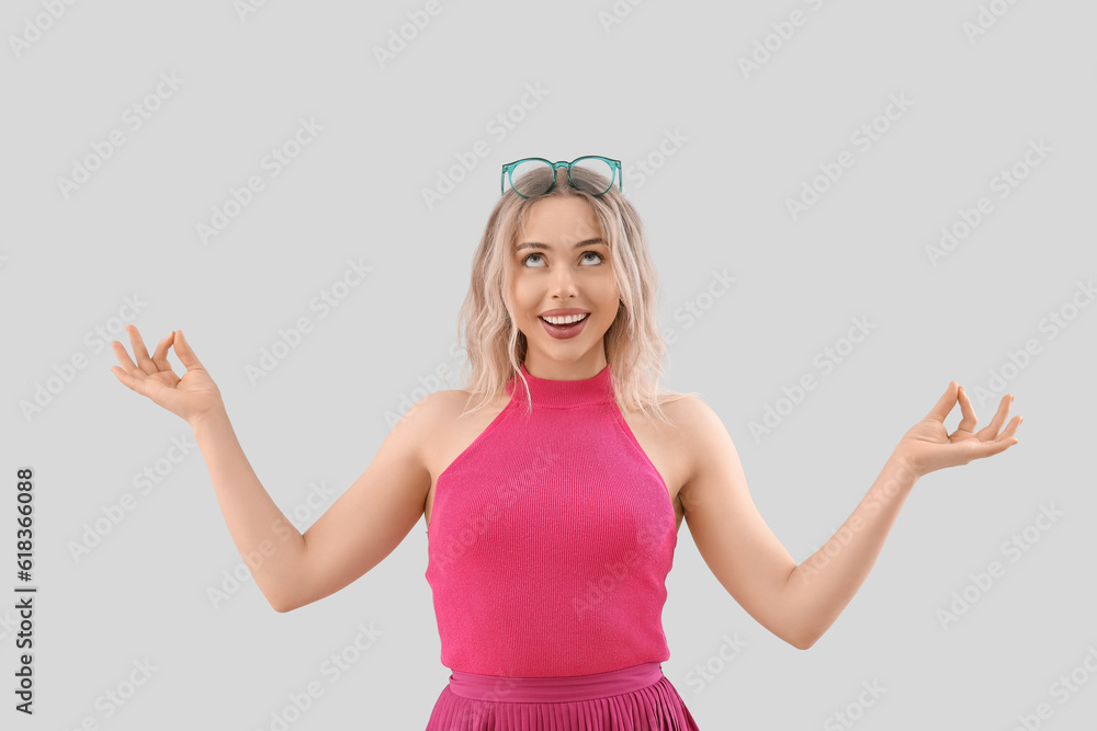 Young woman in stylish eyeglasses meditating on light background