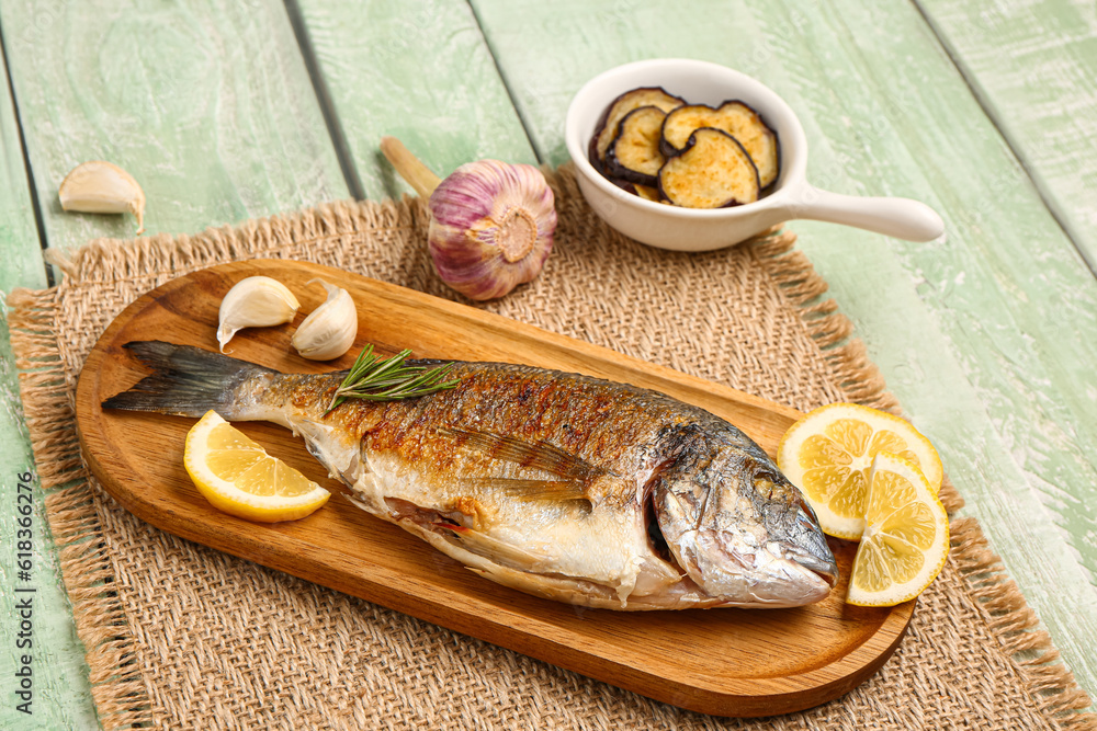 Board with tasty grilled dorado fish on green wooden background